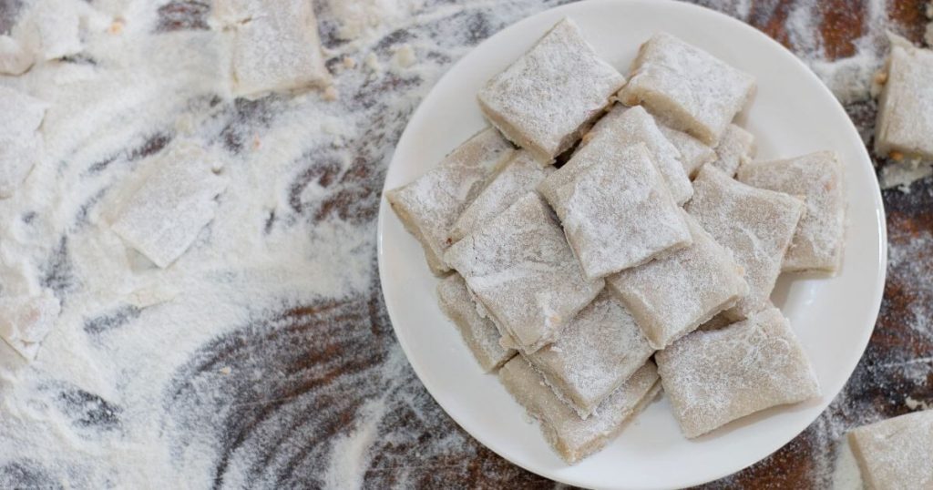 圖中展示了一盤撒滿糖粉的斯里蘭卡甜點Aluwa,周圍是撒在桌面上的糖粉,突顯這道經典甜點的細膩質感。