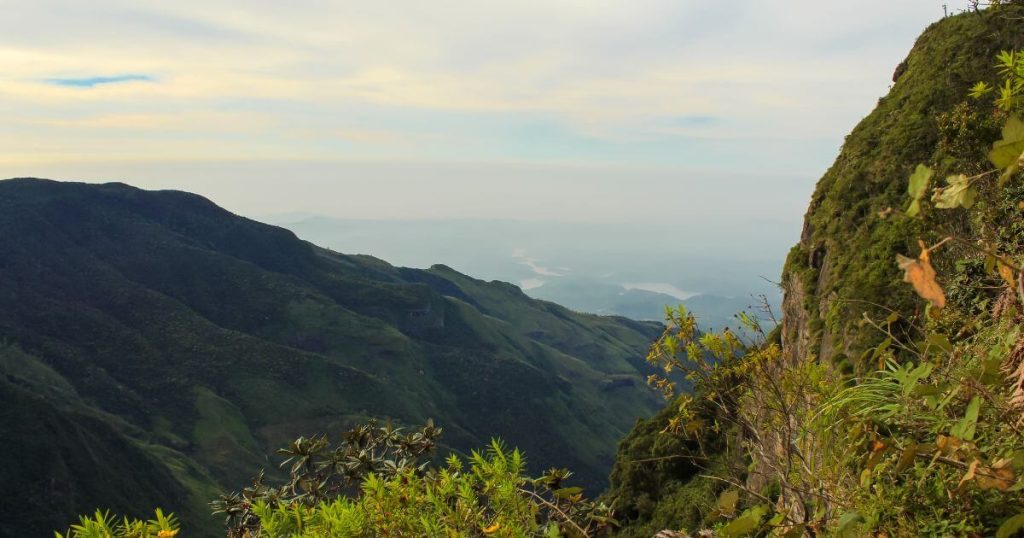 這張照片展示了著名的斯里蘭卡霍頓平原國家公園中的大世界盡頭懸崖,陽光透過山谷,創造出美麗的光影效果,山脈的綠色植被與山谷的深色形成強烈對比。
