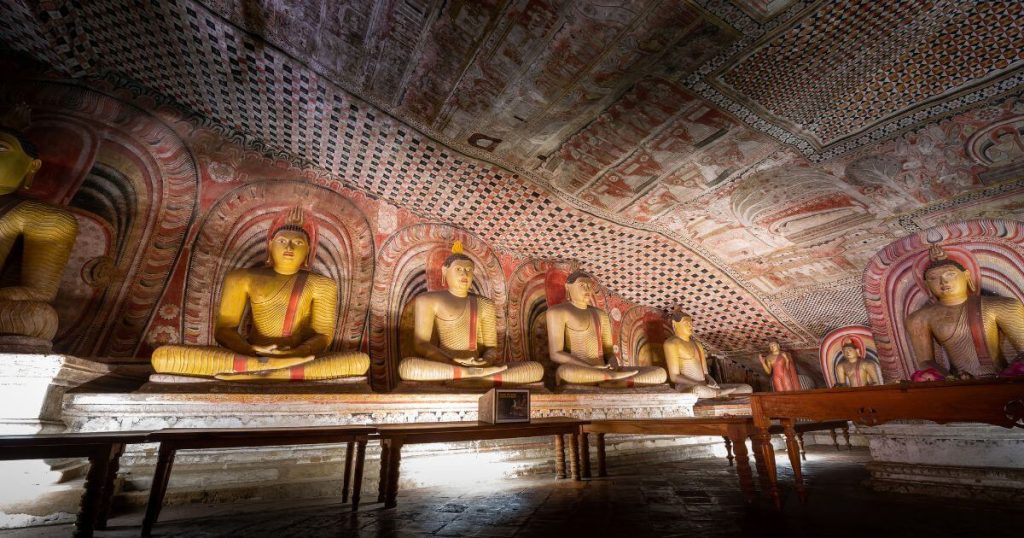 該圖片展示了丹布拉岩洞寺廟內的佛像排列,佛像呈現安詳的坐姿,身後是色彩斑斕且充滿幾何圖案的屋頂壁畫,增添了藝術美感。這些佛像象徵著佛教的信仰與歷史,使人感受到神聖與靜謐的氛圍,是斯里蘭卡宗教建築的重要代表。