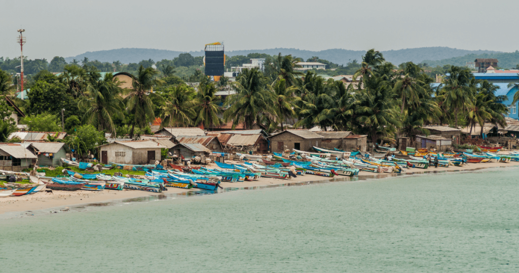 一排色彩繽紛的漁船停靠在斯里蘭卡亭可馬里的沙灘上,後方棕櫚樹與簡樸的房屋,展現出當地平靜的海岸村莊風情。