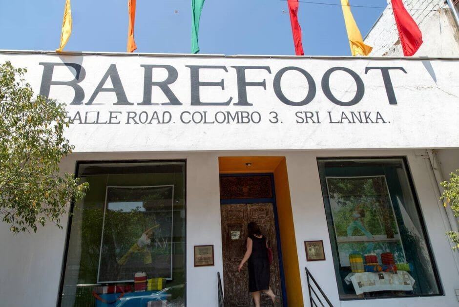 該圖片展示了斯里蘭卡科倫坡的 Barefoot 紡織店正門，位於 Galle Road，店面設計簡約，招牌上清晰標示「BAREFOOT」，並懸掛著鮮艷的旗幟。顧客進入店內，體現該店的熱門購物地點特色。