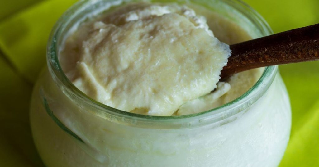 近距離拍攝的一罐濃稠水牛優格,木勺放置在罐內,顯示出優格的細膩與濃厚質地。