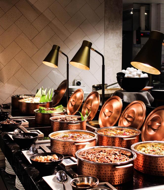 此圖片展示了Courtyard by Marriott Colombo豪華飯店的自助餐區,整齊排列的銅製容器中盛滿了各種美食。黑色石材檯面和金色燈具使整個自助區看起來非常高級且富有現代感。