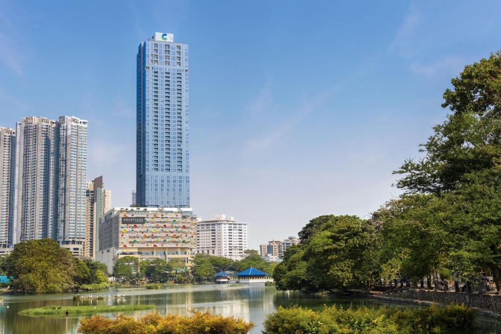 這張圖片展示了Courtyard by Marriott Colombo飯店位於都市中心的高樓外觀,建築外觀高聳且現代,周圍是林立的建築和湖泊,城市天際線與自然景色相互交融,呈現出一幅美麗的城市景觀。