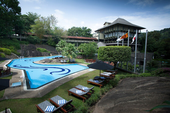 康提飯店擁有一個造型獨特的泳池，周圍被綠樹和旗幟環繞，設施齊全，提供舒適的休閒體驗。