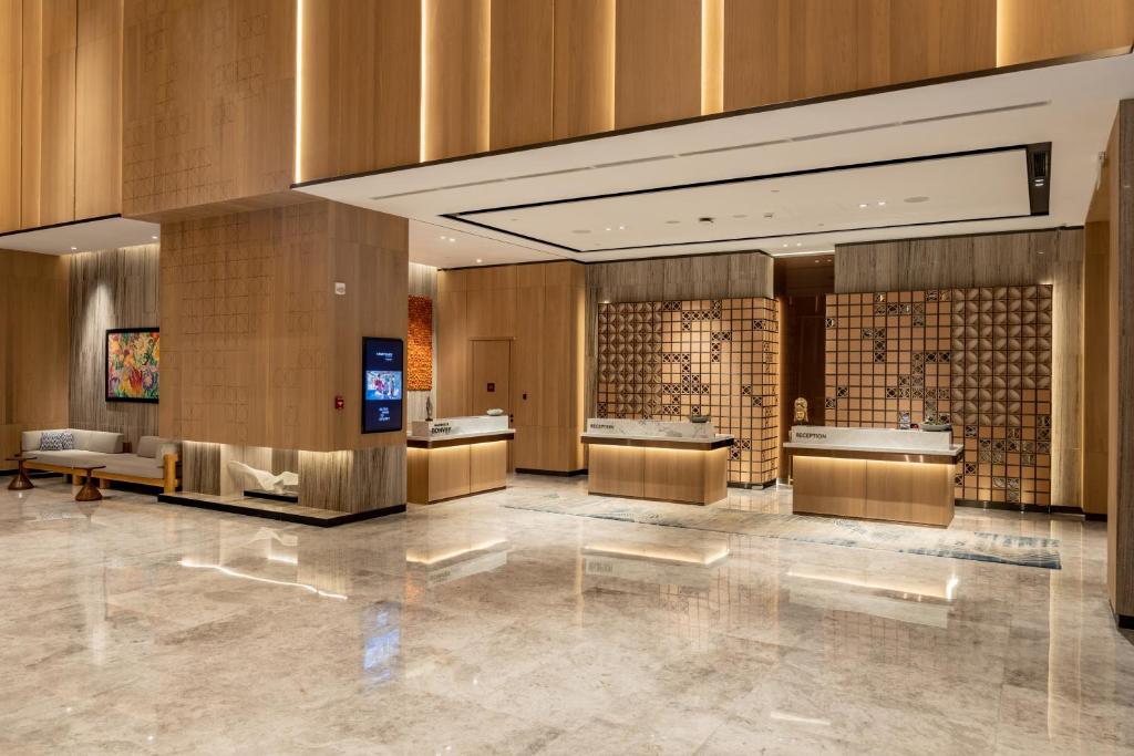 此圖片展示了Courtyard by Marriott Colombo的現代化豪華飯店大廳,設計簡約高雅,牆面與接待櫃台運用木質材質,搭配間接照明,營造出舒適且典雅的氛圍。櫃台旁的藝術畫作和休息區的沙發,使空間更具品味。