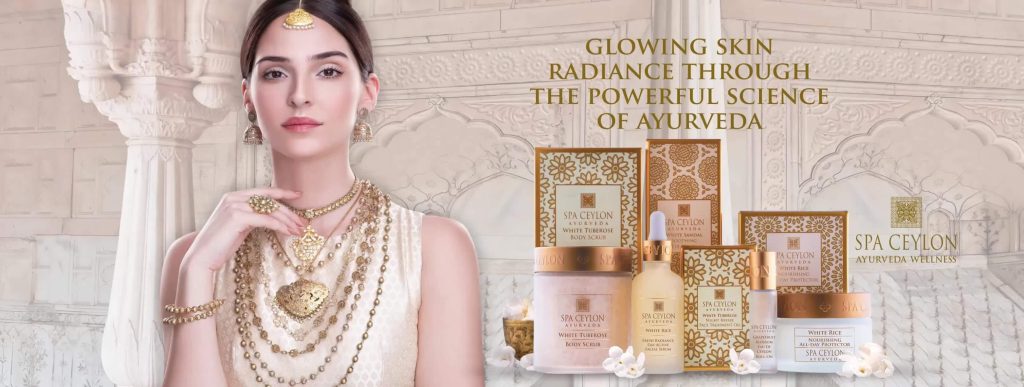 一位穿著傳統金色紗麗的女性模特,背景是白色的傳統建築,旁邊展示了一系列SPA Ceylon Ayurveda護膚產品。