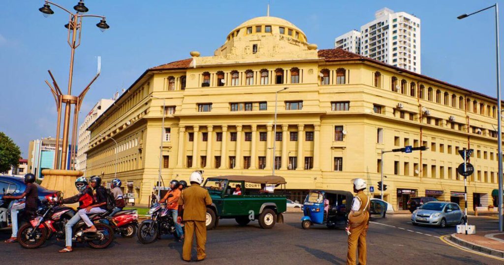 該圖片展示了斯里蘭卡可倫坡著名的Galle Road街景,一座古老的黃色建築物矗立於路口,周圍環繞著摩托車、嘟嘟車和汽車,展現了這座城市的交通風貌。