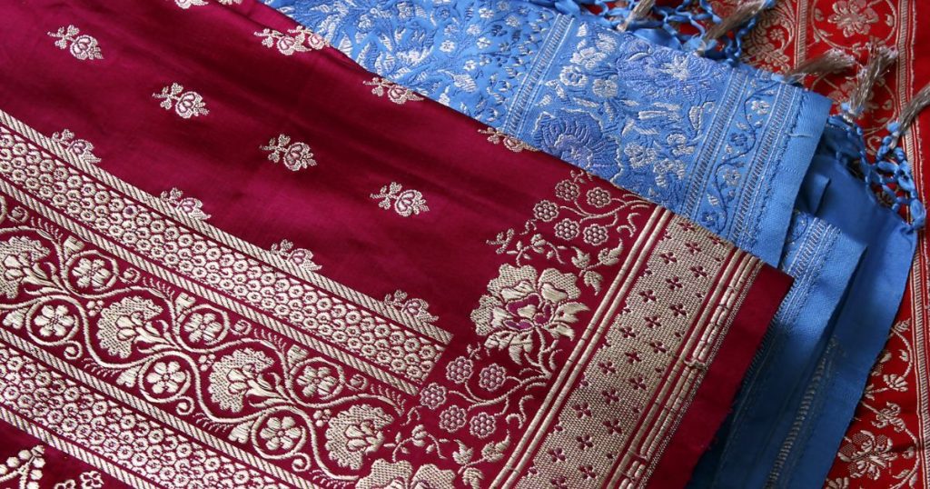 紅色與藍色的精美布料,搭配著金色花卉和幾何圖案,代表傳統紗麗手工織品的優雅風采。