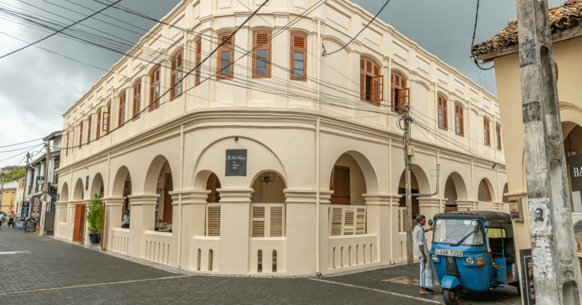 這張圖片展示了斯里蘭卡加勒(Galle)的街道,畫面中可見一輛藍色的三輪車(嘟嘟車)停在街角。旁邊是經典的殖民風格建築,展現出當地獨特的歷史與文化氛圍。街道上有一些當地人和商店,整體氛圍輕鬆又富有生活氣息,這是加勒古城的典型景象。