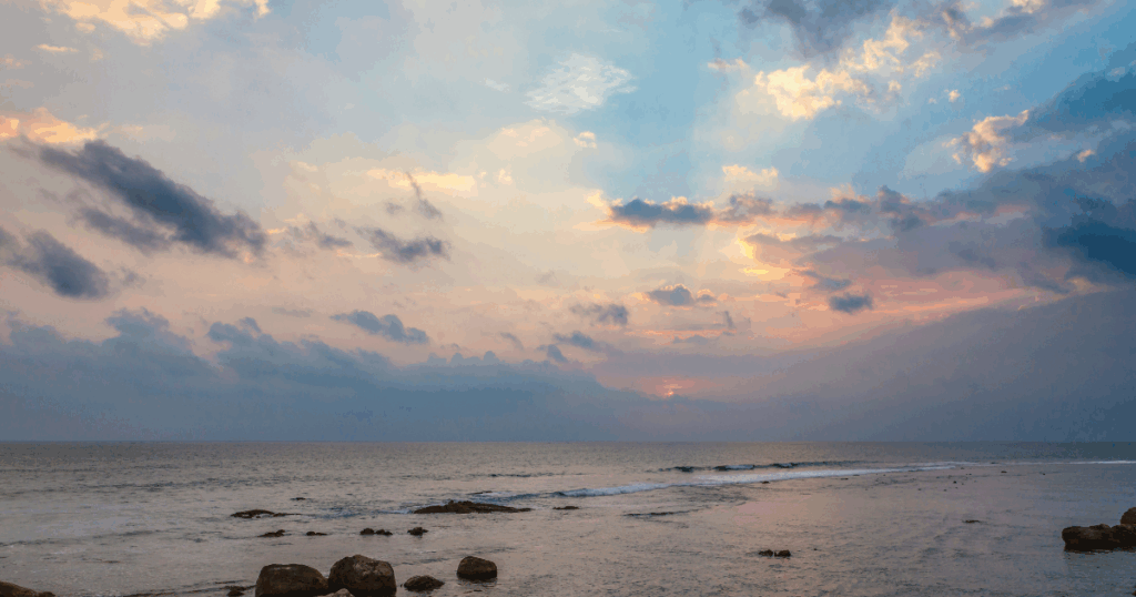 這張圖片捕捉了斯里蘭卡加勒海岸的壯麗日落景象,夕陽的光線透過雲層洒向海面,營造出溫暖而平靜的氛圍。海浪輕拍沙灘,遠處的天際線漸漸被暮色覆蓋,畫面展現出這個熱帶地區的自然美景。