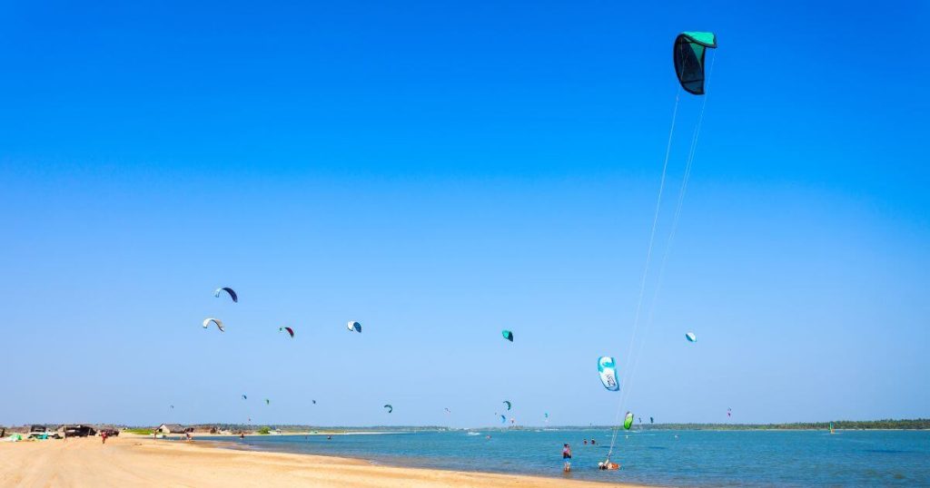 圖片展示斯里蘭卡卡爾皮蒂耶的美麗沙灘,碧藍的天空與海面上點綴著多彩的風箏,風箏衝浪者在清澈的水域中享受活動的樂趣。遠處的沙灘和茅草屋增添了一份自然的魅力,展現出這個熱門旅遊地點的動感與活力。