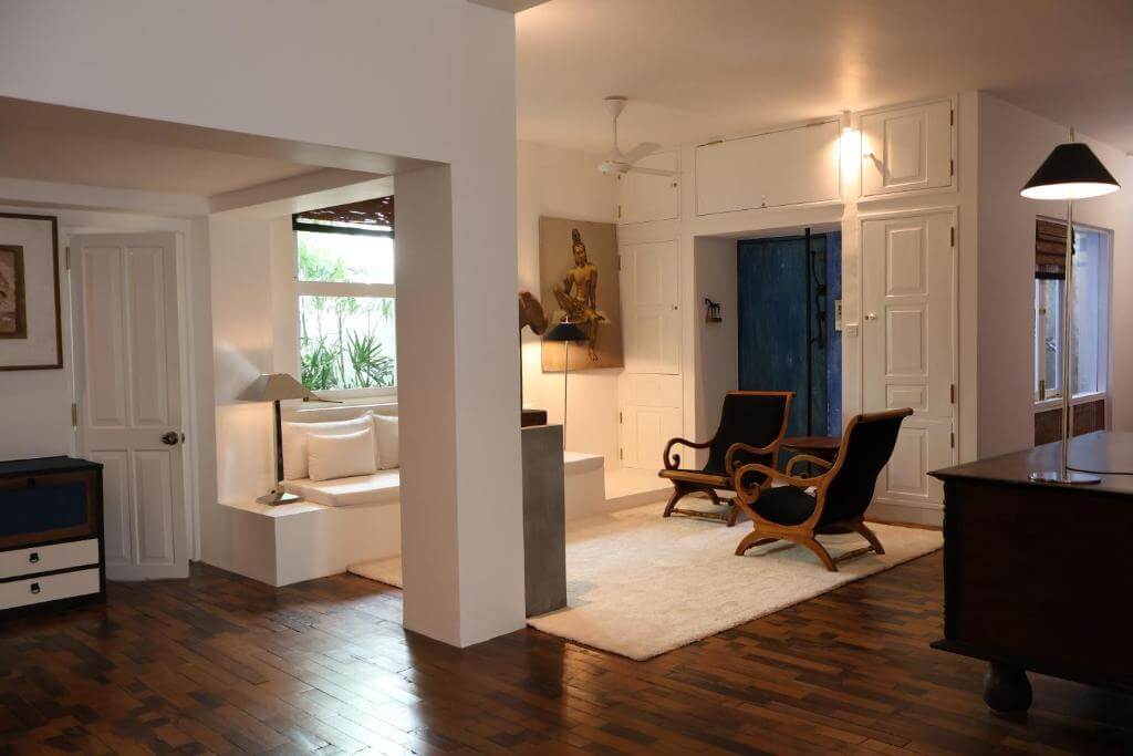 照片展示了斯里蘭卡建築師Geoffrey Bawa位於可倫坡的故居(Home No.11)室內一隅,整體設計簡約而優雅,融合自然光與空間感。木質地板與白色牆面營造溫潤氛圍,牆上掛有佛像畫作,兩張古典木質休閒椅置於米色地毯上,角落還設有舒適的窗邊臥榻,呈現Bawa「熱帶現代主義」的設計理念。這裡不僅是建築迷必訪之地,更展現其將現代與傳統結合的獨到美學。